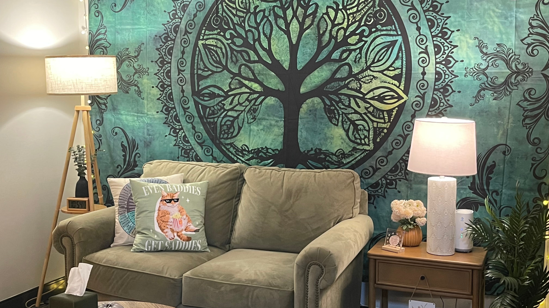 Cassidy's therapy office: a soft green couch with playful pillows beneath a tree-of-life tapestry and warm lamplight